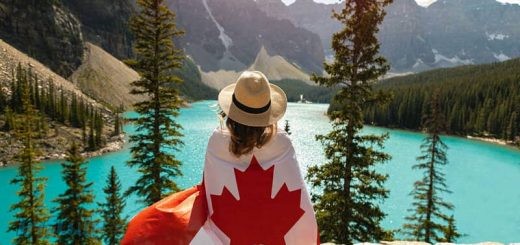 A person with a flag wrapped around her shoulders looking at a lake Description automatically generated